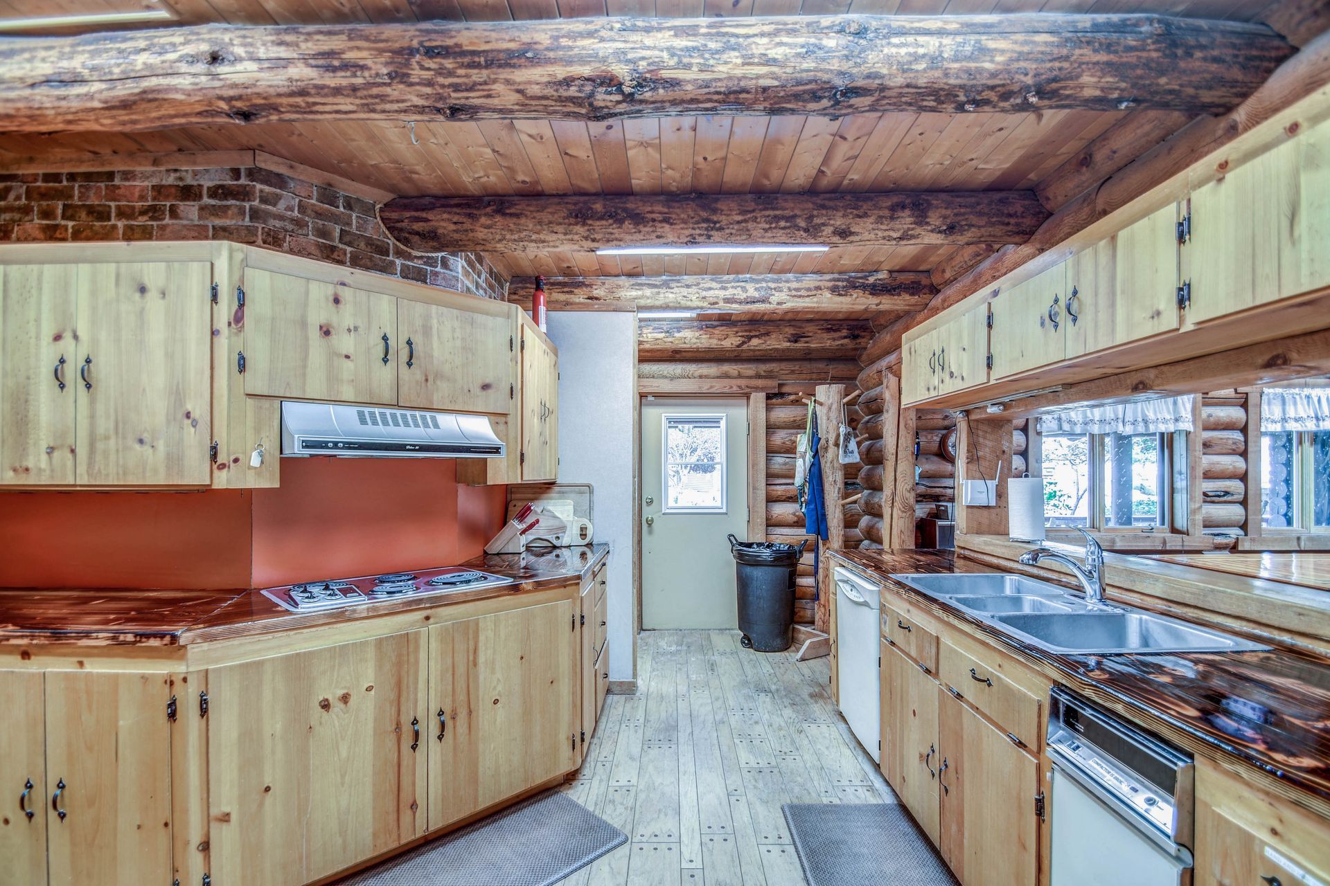 Rustic log cabin kitchen with wooden cabinets, red countertops, and a central walkway