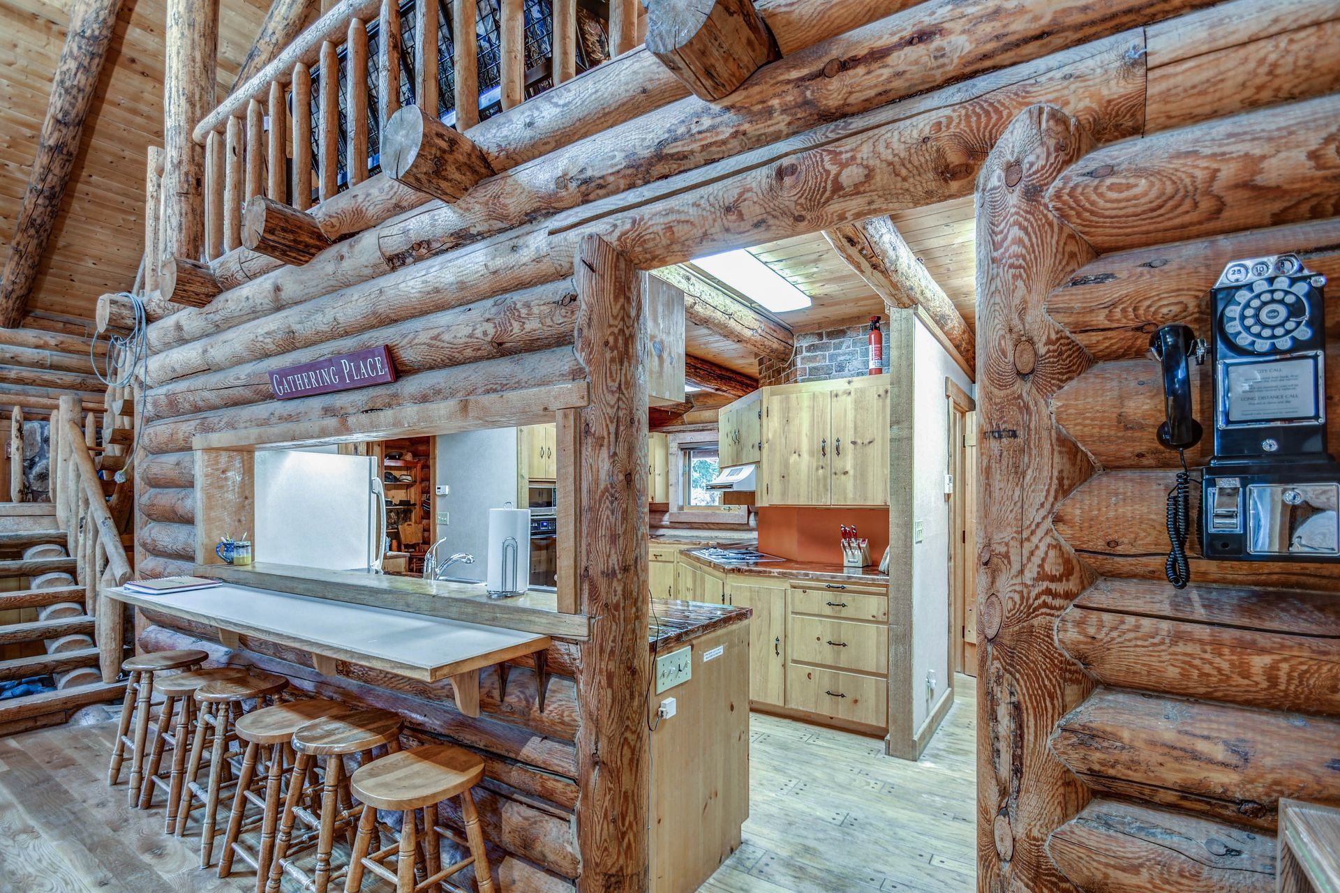 Rustic log cabin interior with wooden bar stools, staircase, and bright kitchen area