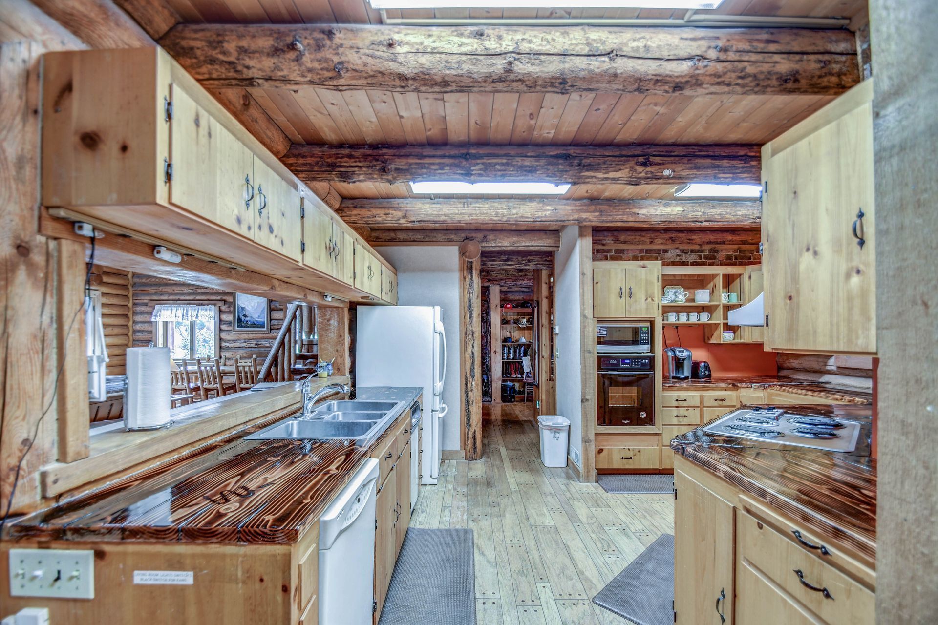 Wood-paneled kitchen with unfinished cabinets, exposed ceiling beams, and marble-patterned counters.