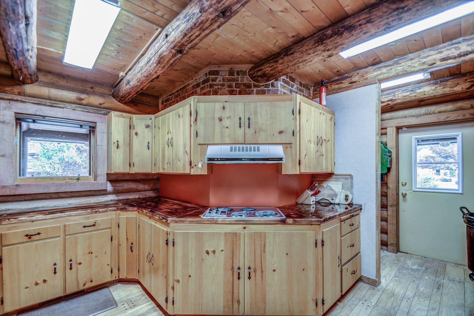 Rustic kitchen with wood-paneled walls, light cabinets, red backsplash, and skylights