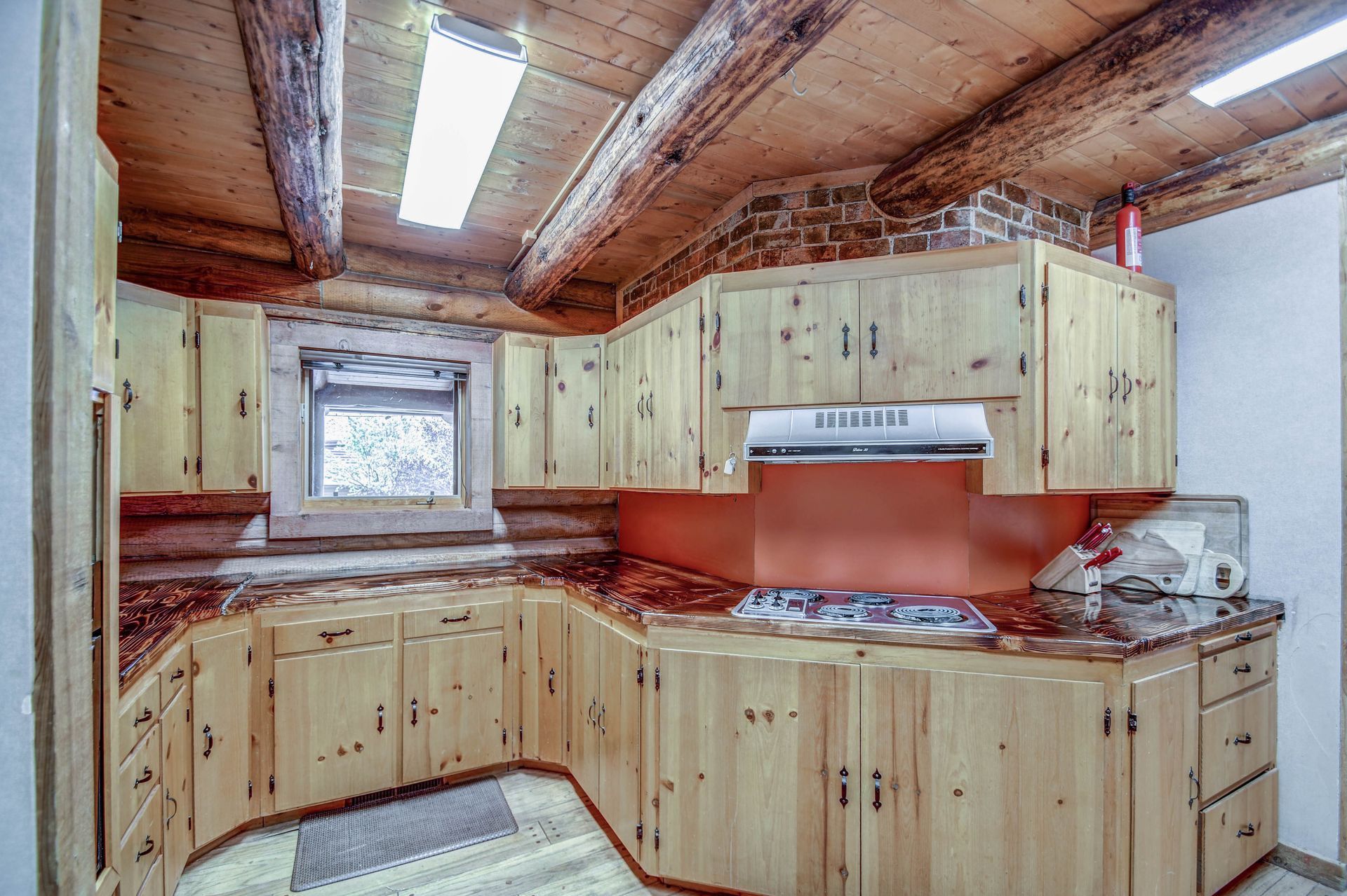 Wood-paneled kitchen with light cabinets, red backsplash, and a skylight above the stove.