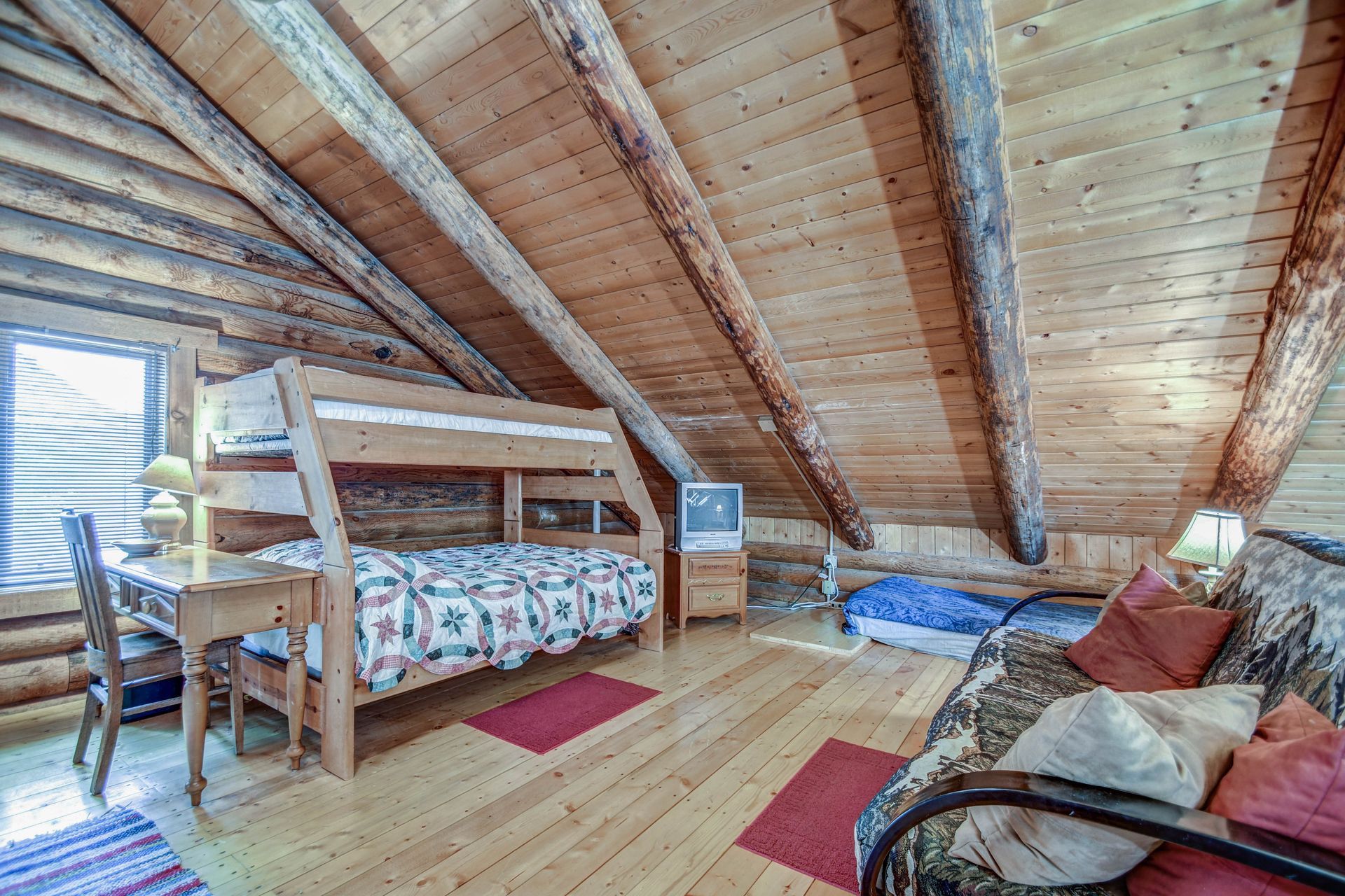 Loft bedroom with wooden beams, twin beds, desk, and skylight windows