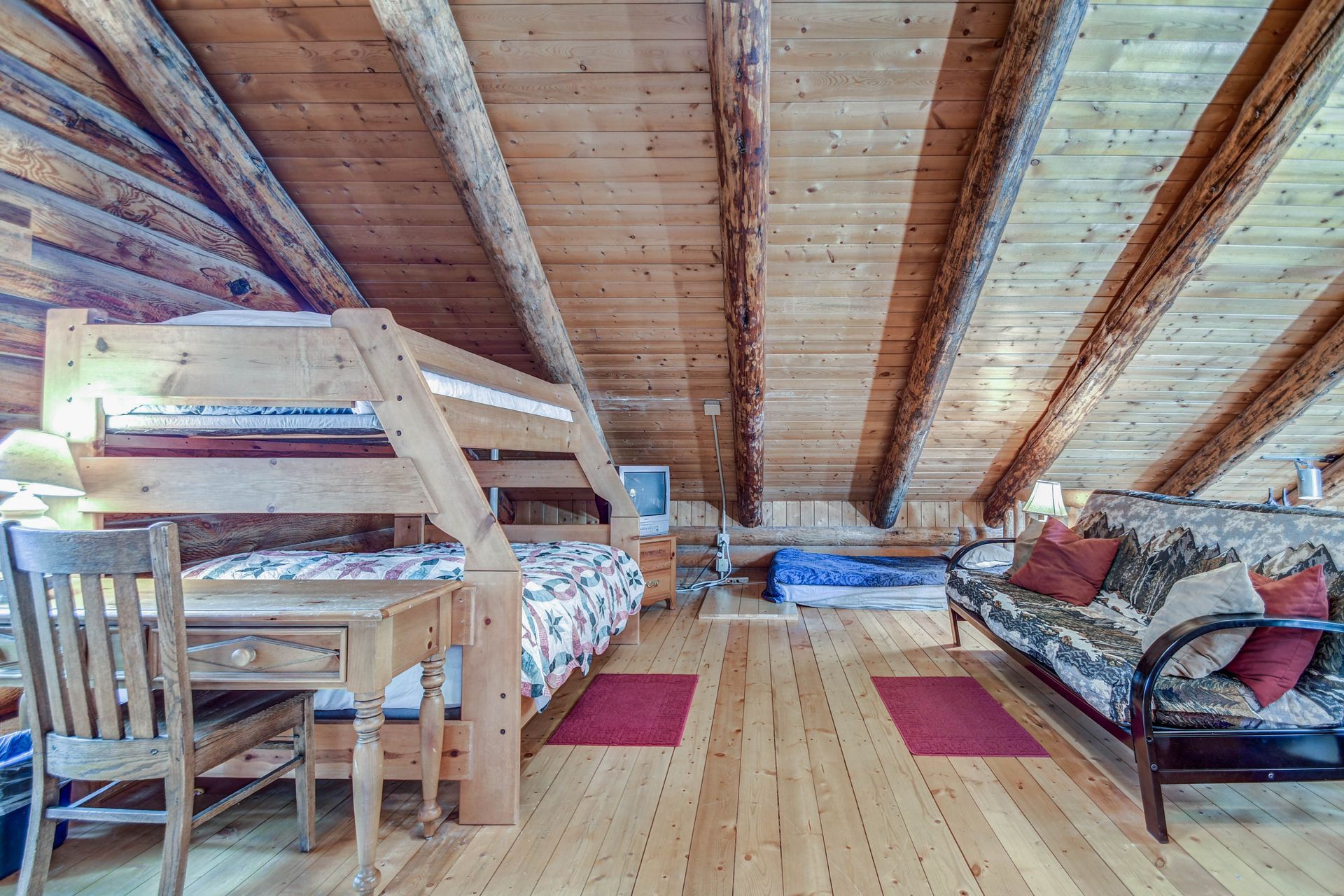Cozy attic bedroom with wooden beams, two beds, and a desk on a light wood floor.