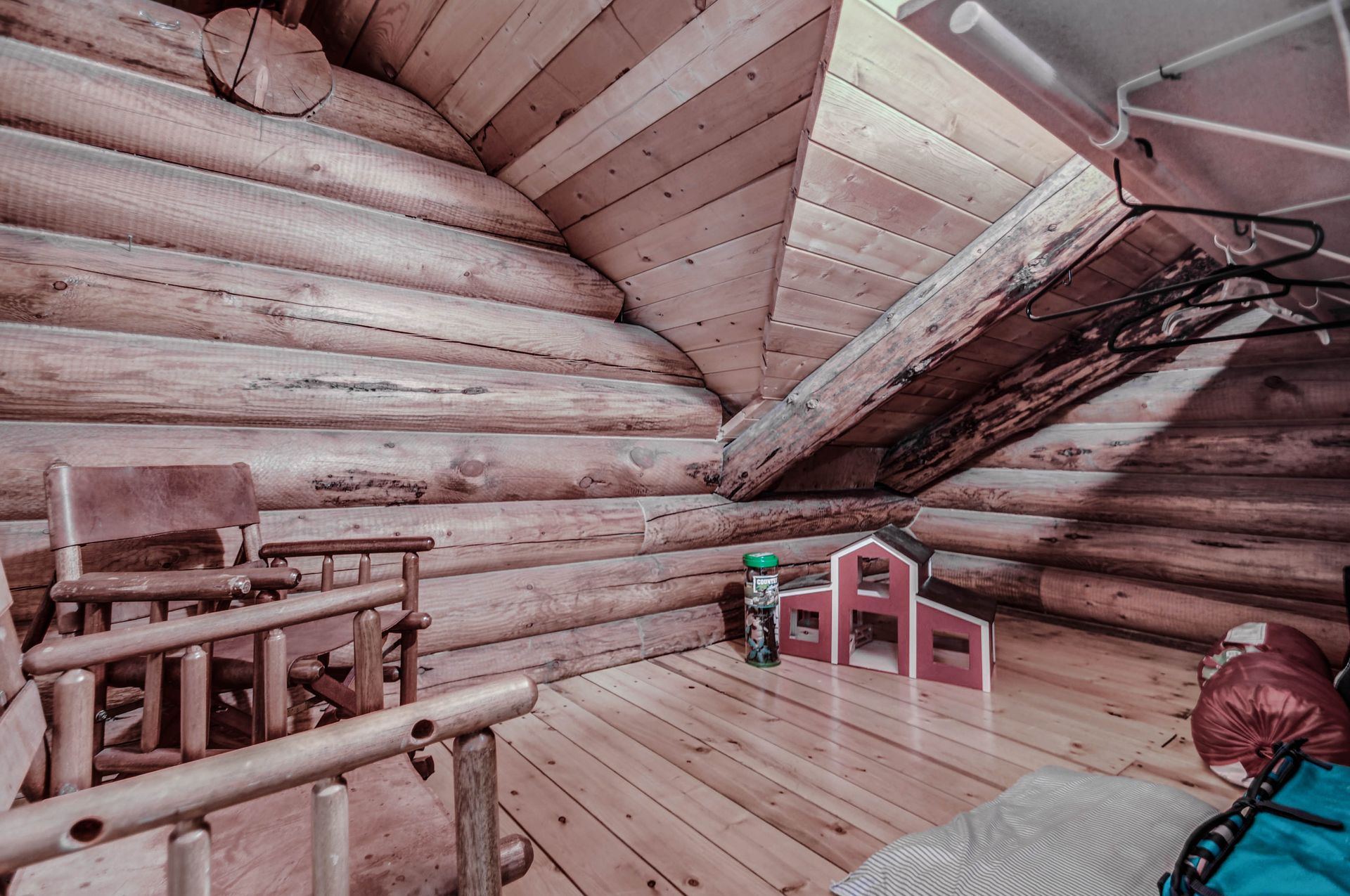 Attic playroom in a log cabin with wooden floor, slanted ceiling, and toy chairs near a small child figurine.