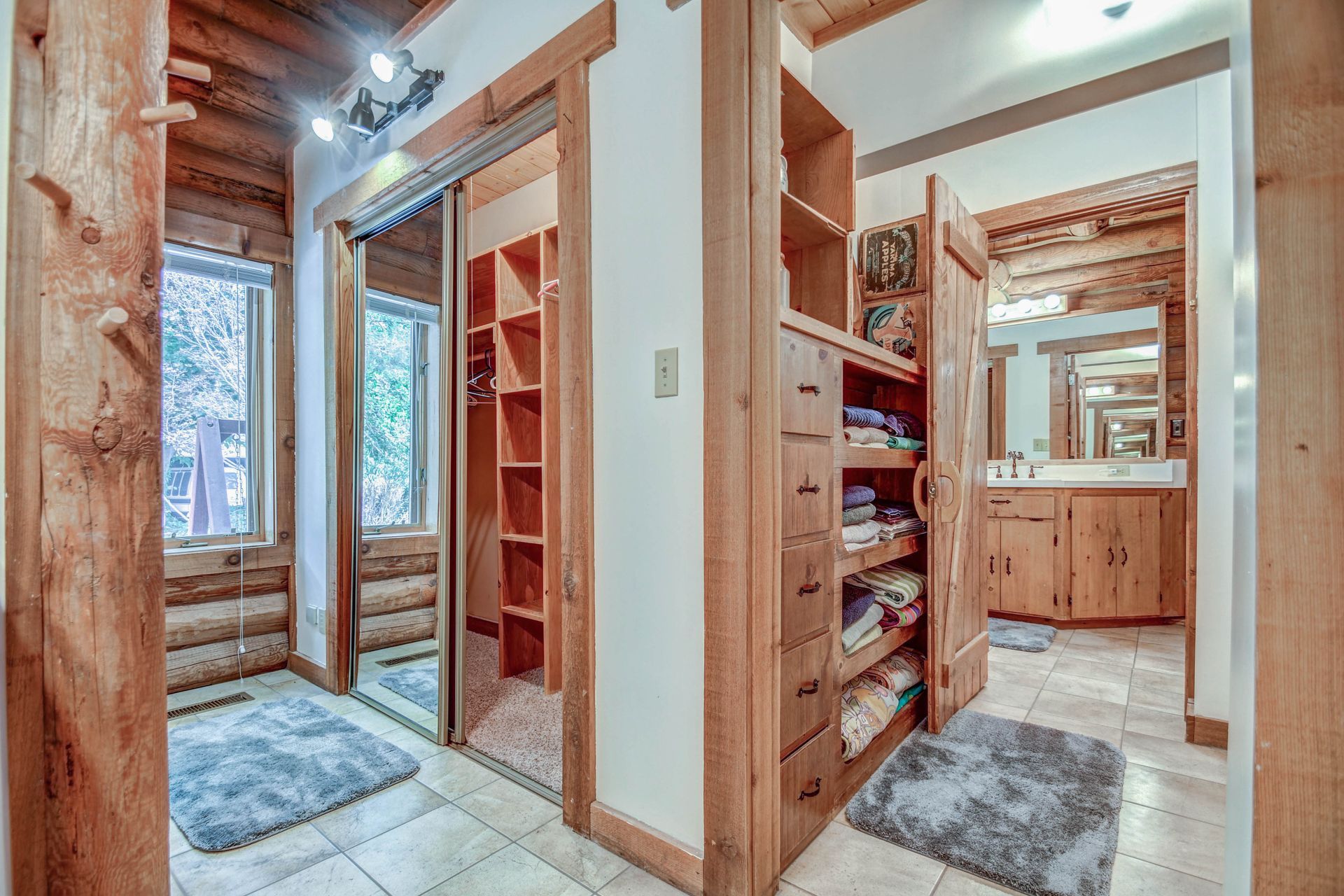Wood-paneled hallway with built-in shelves, tiled floor, and mirrors reflecting a bathroom vanity.