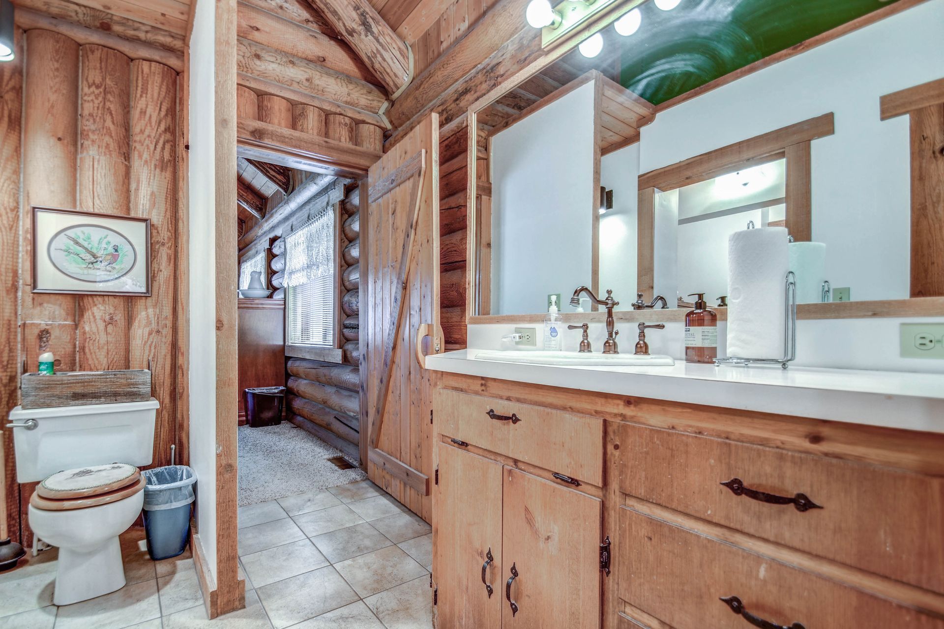 Rustic bathroom with wood-paneled walls, toilet, double sink vanity, and large mirror