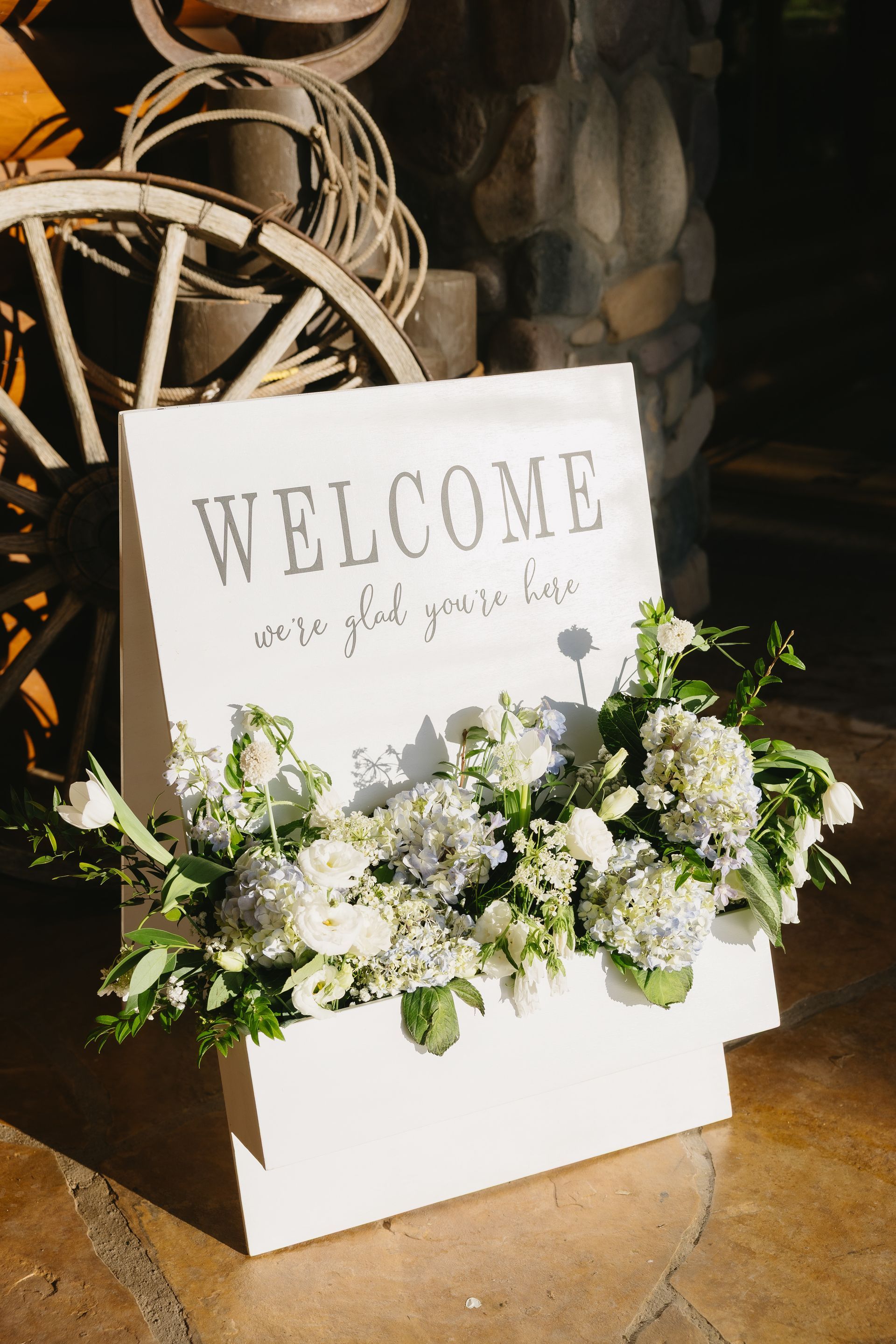 White floral arrangement in a box with a “WELCOME” sign on a rustic wooden floor