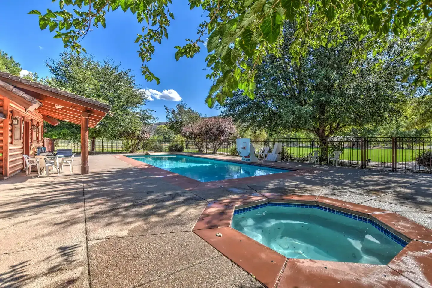 Swimming pool and hot tub next to a house with trees on a sunny day.