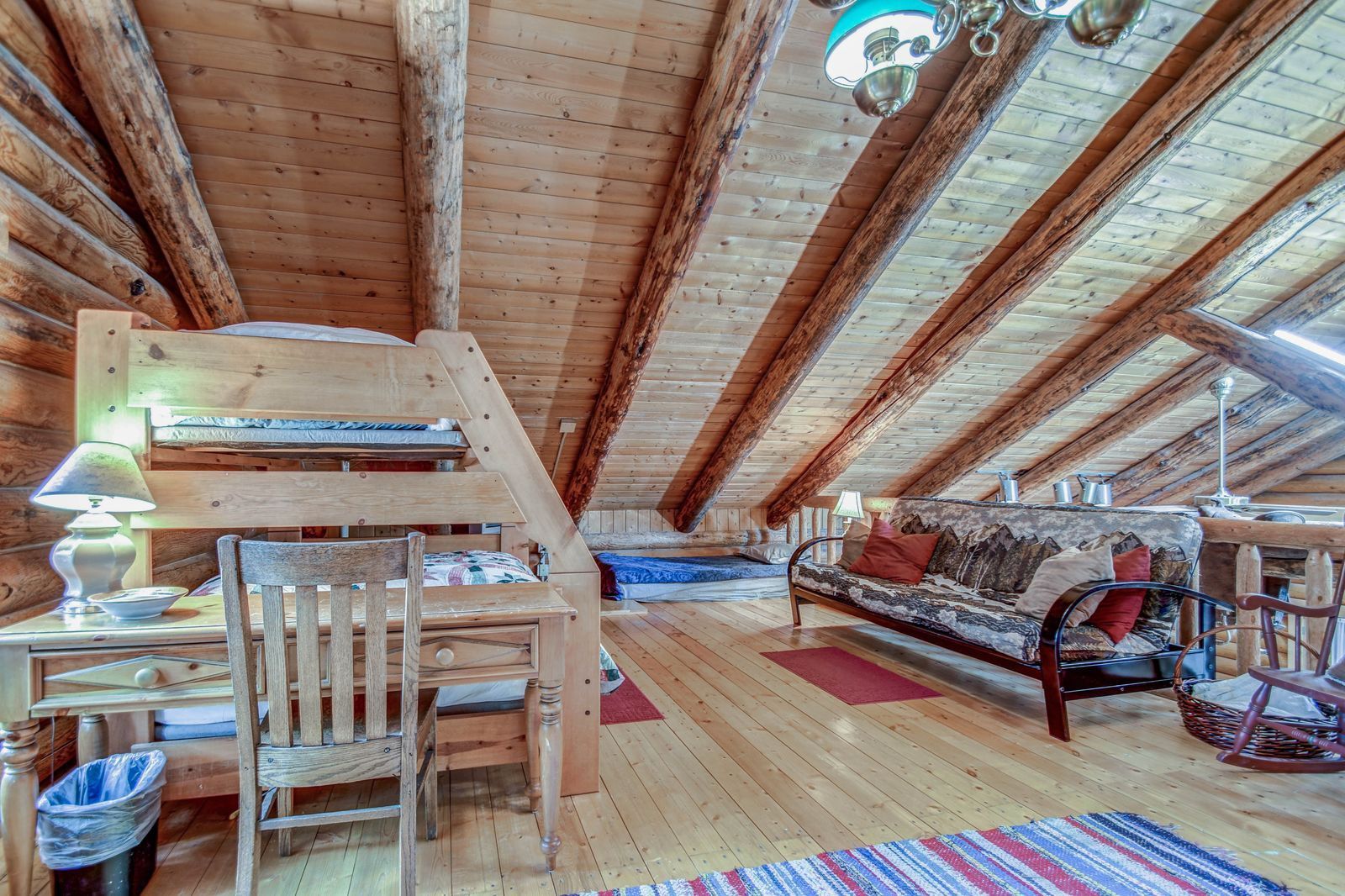 Rustic loft bedroom with exposed wooden beams, a bed, desk, sofa, and patterned rugs