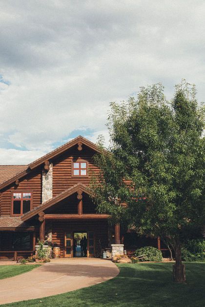 Rustic wooden lodge with a covered entrance and large tree in front under a cloudy sky