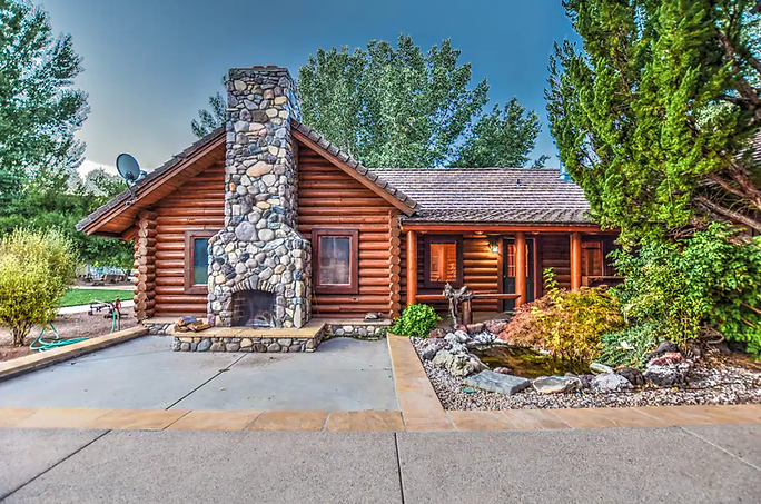 Log cabin with stone chimney, small pond, and trees.