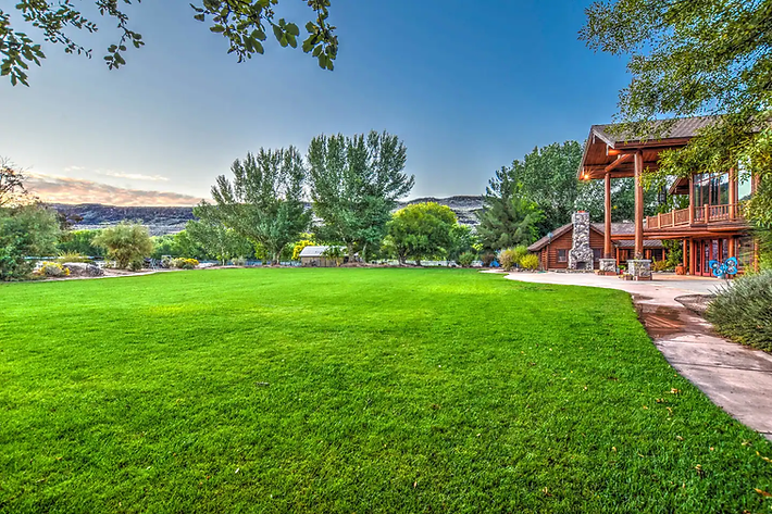 Lush green lawn beside a river, with trees, blue sky, and a wooden deck on the right.