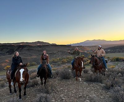 Four riders on horses in a desert at dusk, with mountains and a fading sunset in the background