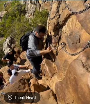 People rock climbing a steep cliff with chain holds at Lion’s Head