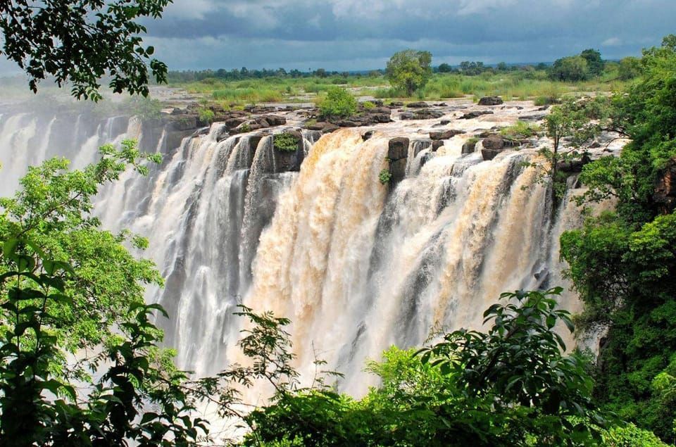 A waterfall is surrounded by trees and a cloudy sky