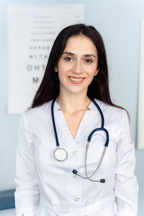 Smiling doctor in white coat with stethoscope standing in a bright clinic office