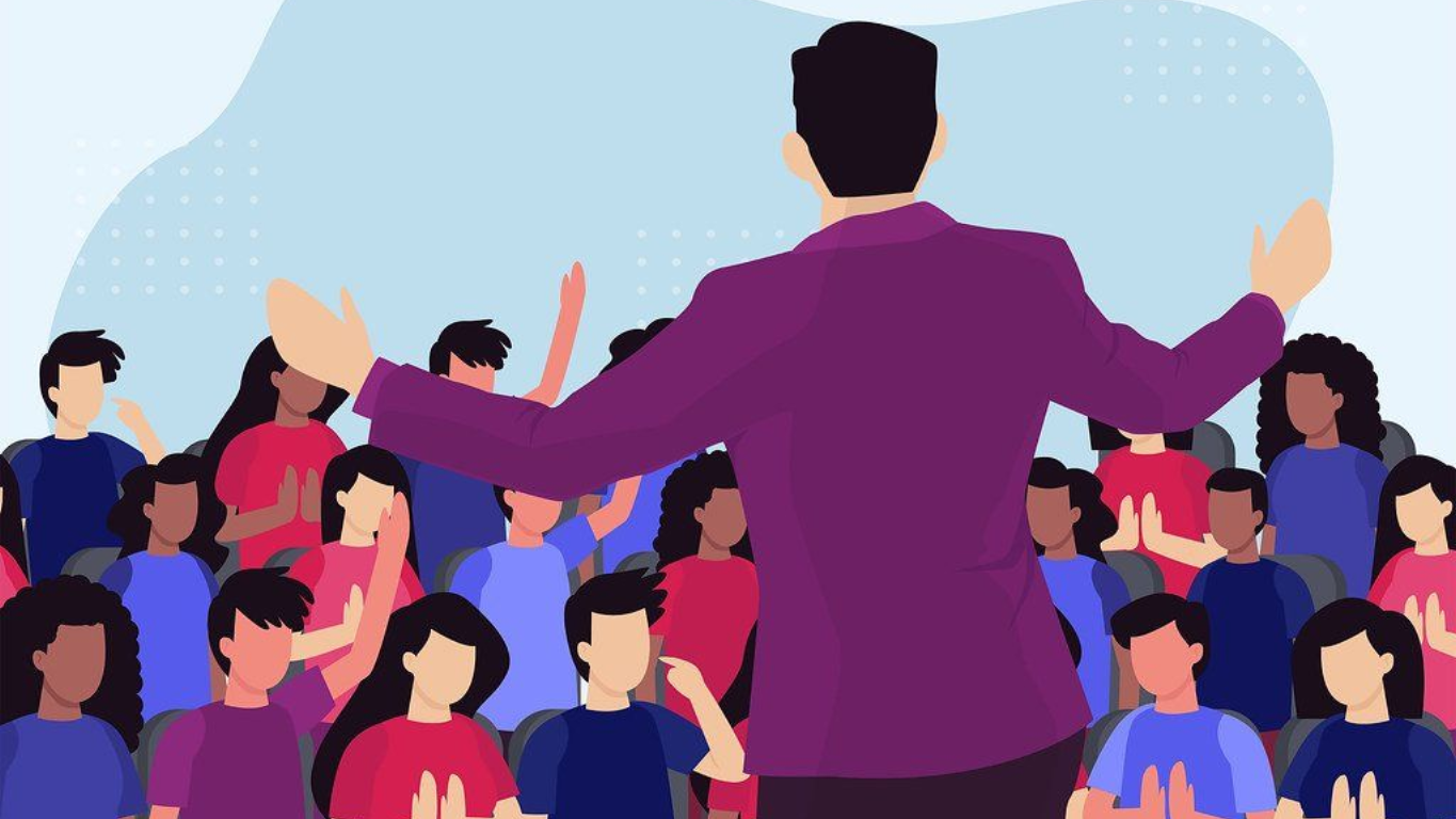 Man in purple suit speaking to a diverse crowd with raised arms, blue sky backdrop.