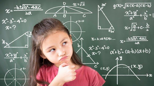 Girl looking at math equations on a chalkboard, appearing thoughtful.