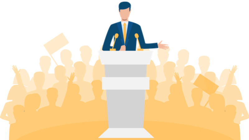 Man speaking at podium, gesturing to crowd of silhouettes holding signs, yellow tones.