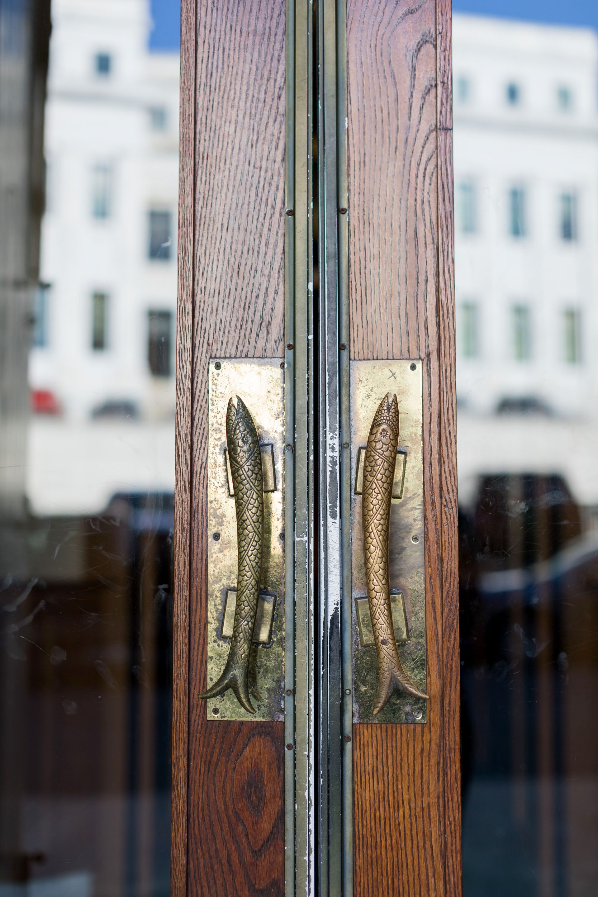 Close-up of wooden double doors with brass handles and blurred buildings reflected in the glass.