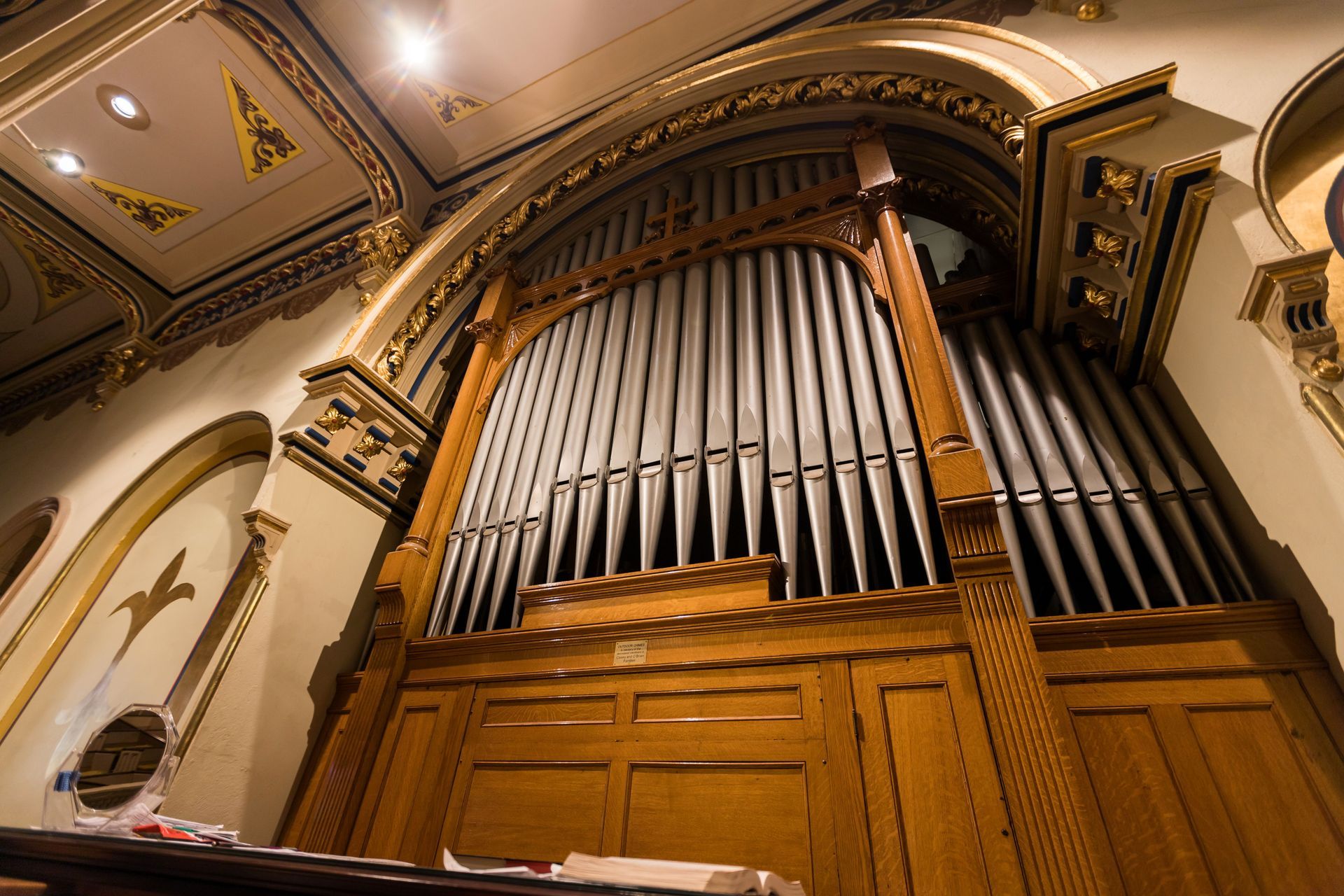 Large pipe organ in a ornate church interior, viewed from below with arched ceiling details