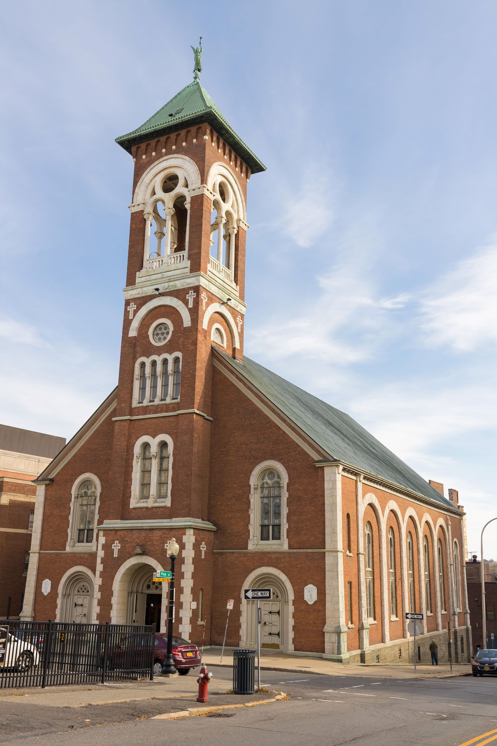 Red-brick church with tall clock tower and green roof on a street corner under a blue sky