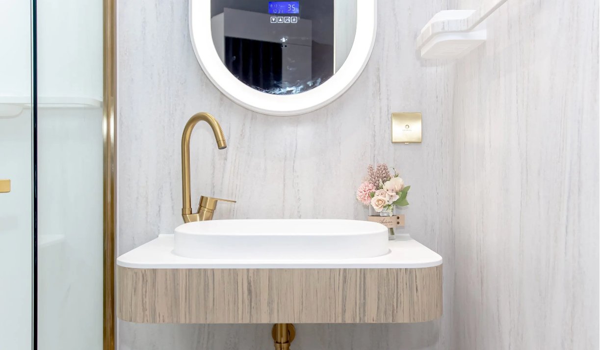 Modern bathroom vanity with round mirror, brass faucet, white sink, and light wood paneling