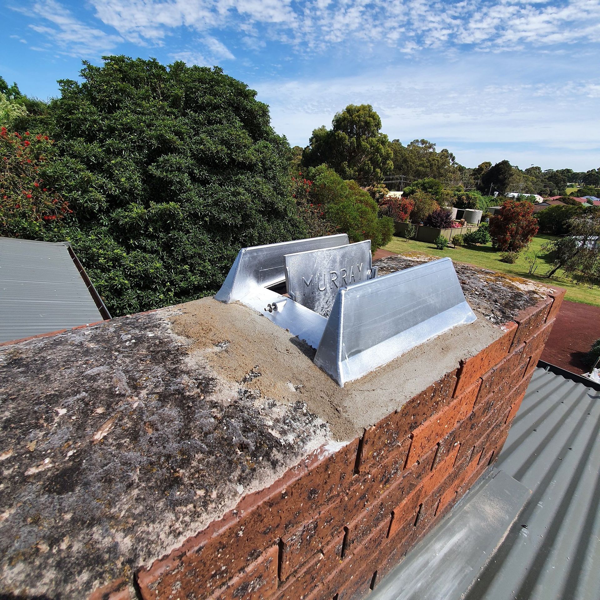 A brick chimney on top of a roof with trees in the background