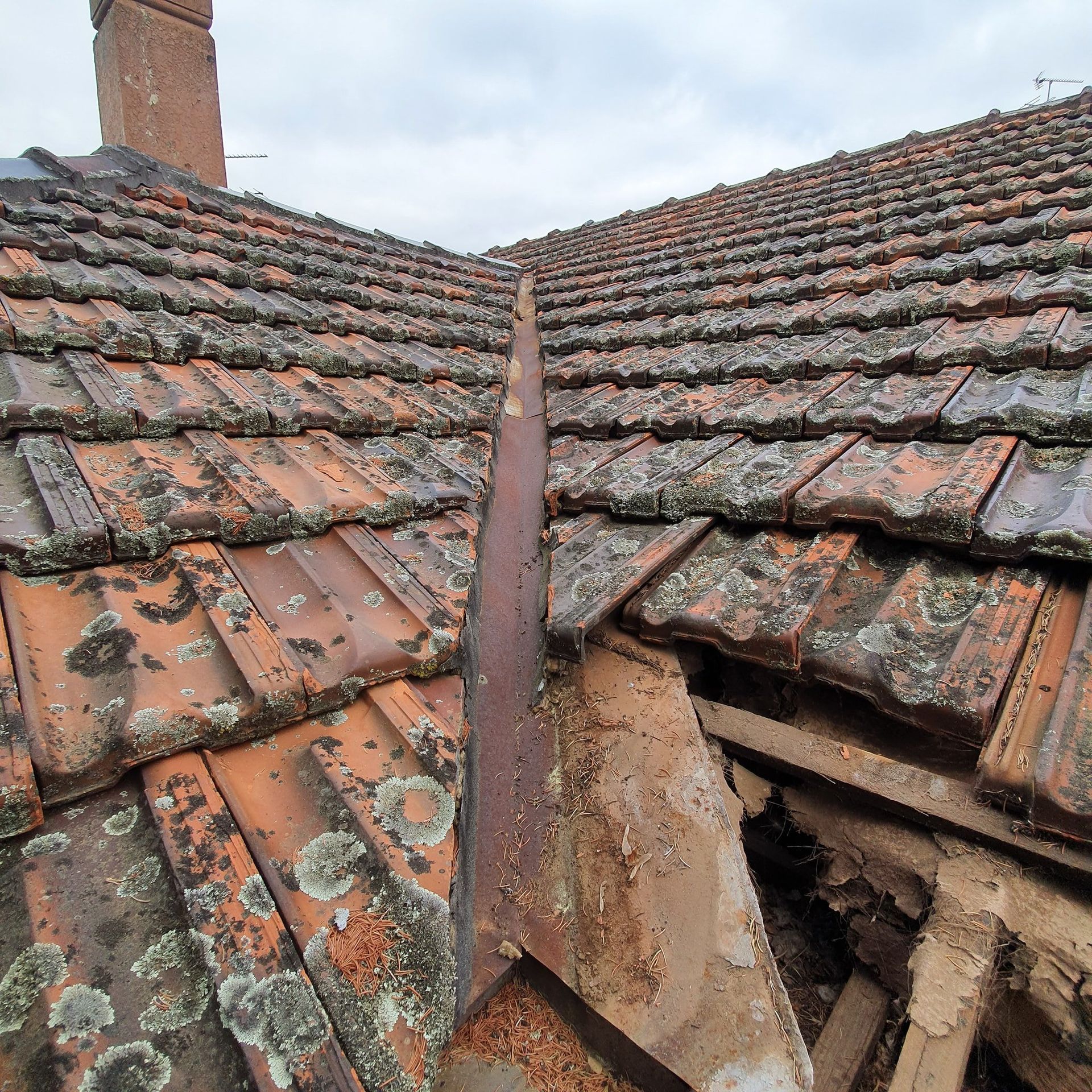 A roof with a lot of tiles and a chimney in the background.