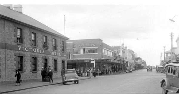 A black and white photo of a city street with a victoria hotel in the background. A black and white photo of a city street with a victoria hotel in the background.