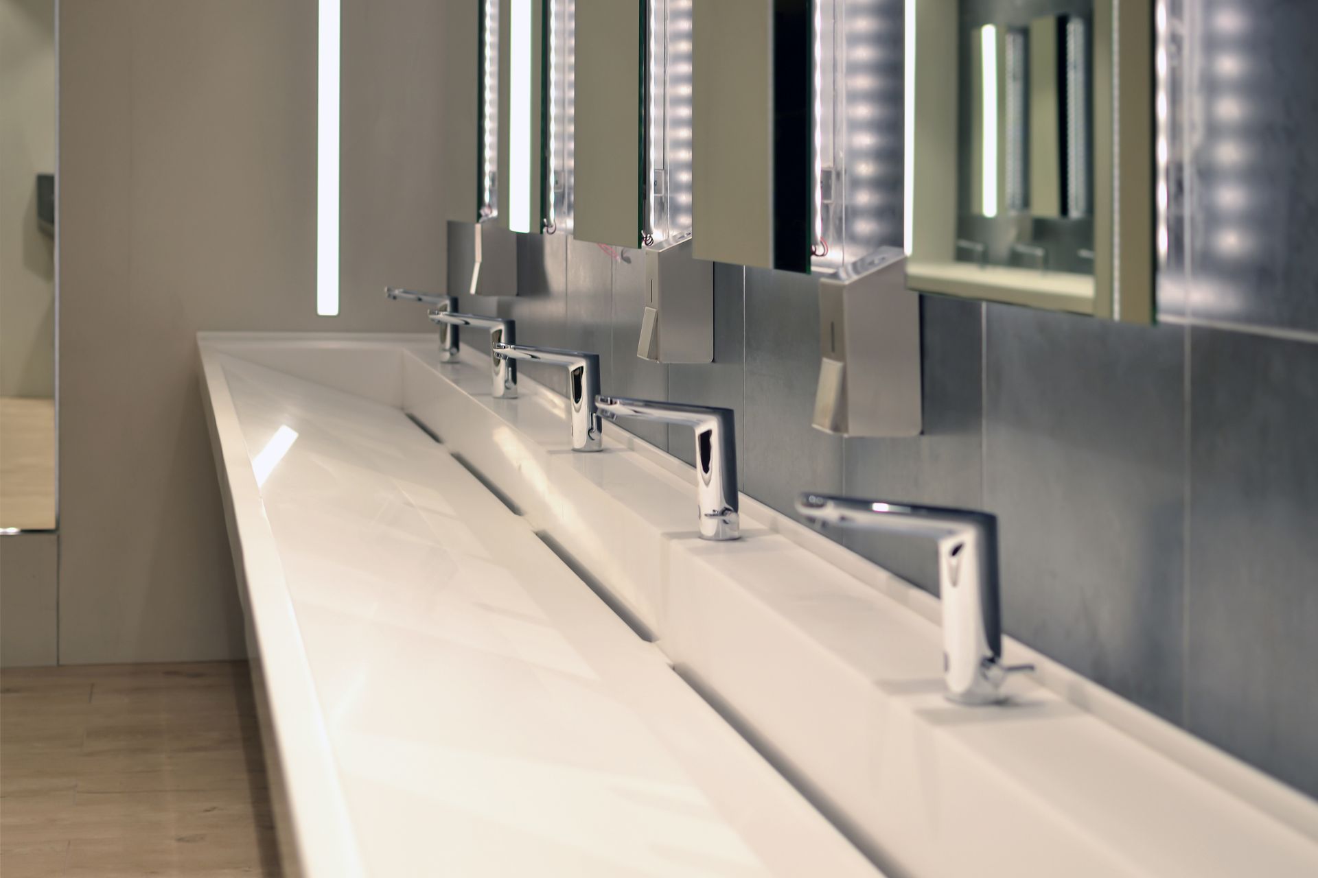 A row of commercial sinks with mirrors in a commercial bathroom. A row of commercial sinks with mirrors in a commercial bathroom.