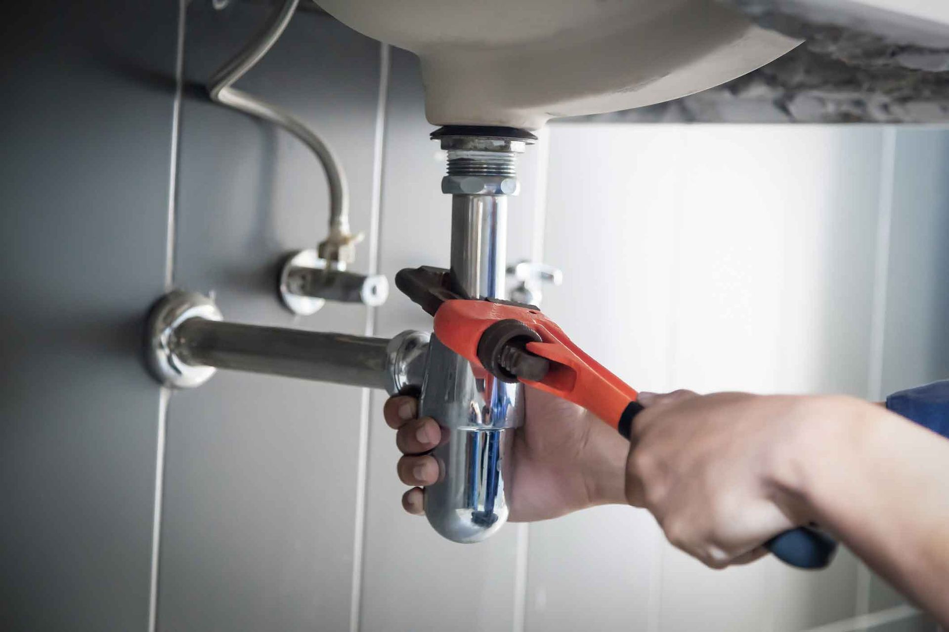 A plumber is fixing a sink pipe with a wrench.
