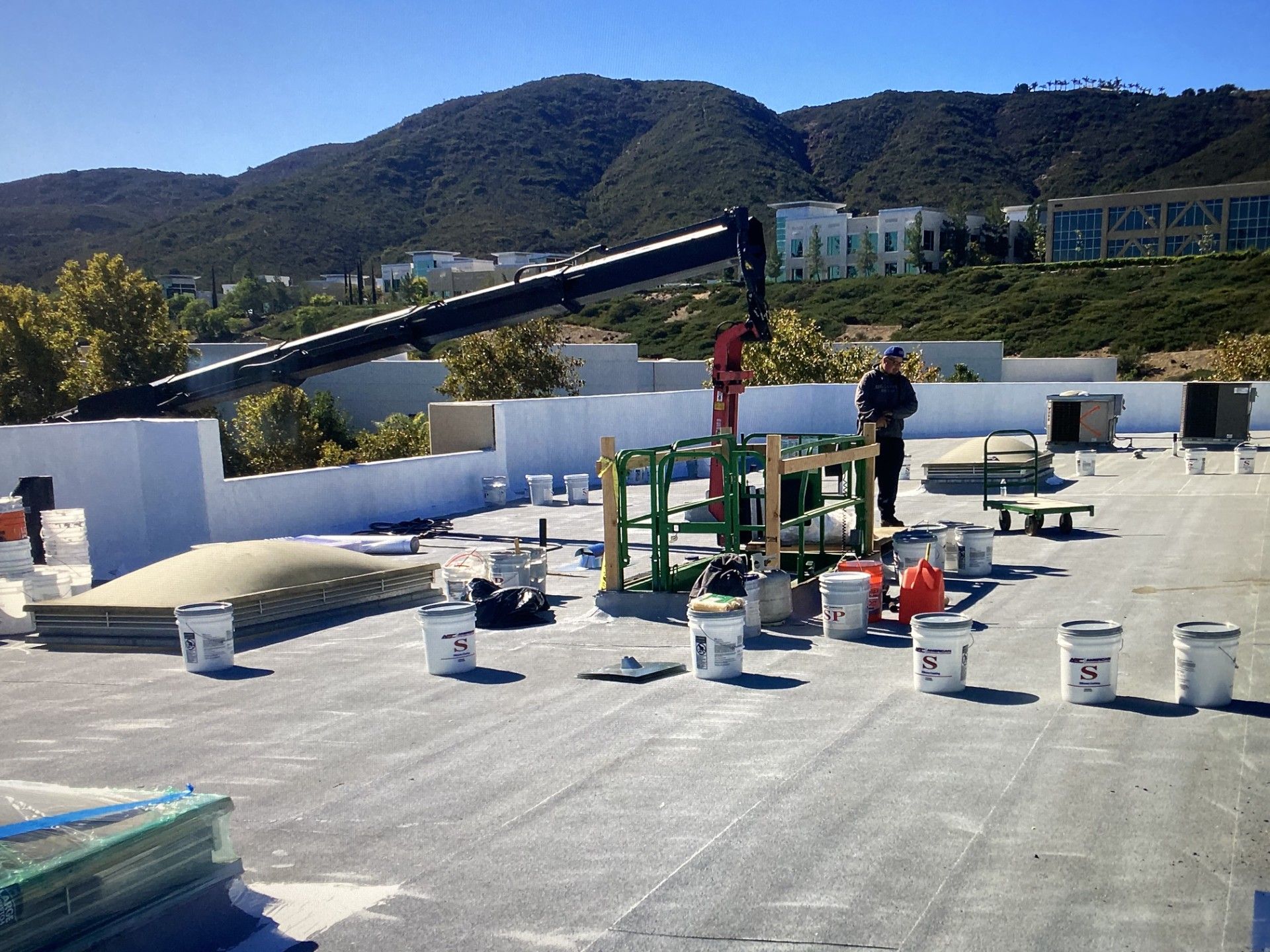 Rooftop construction site with workers, crane arm, and buckets under clear skies near hills