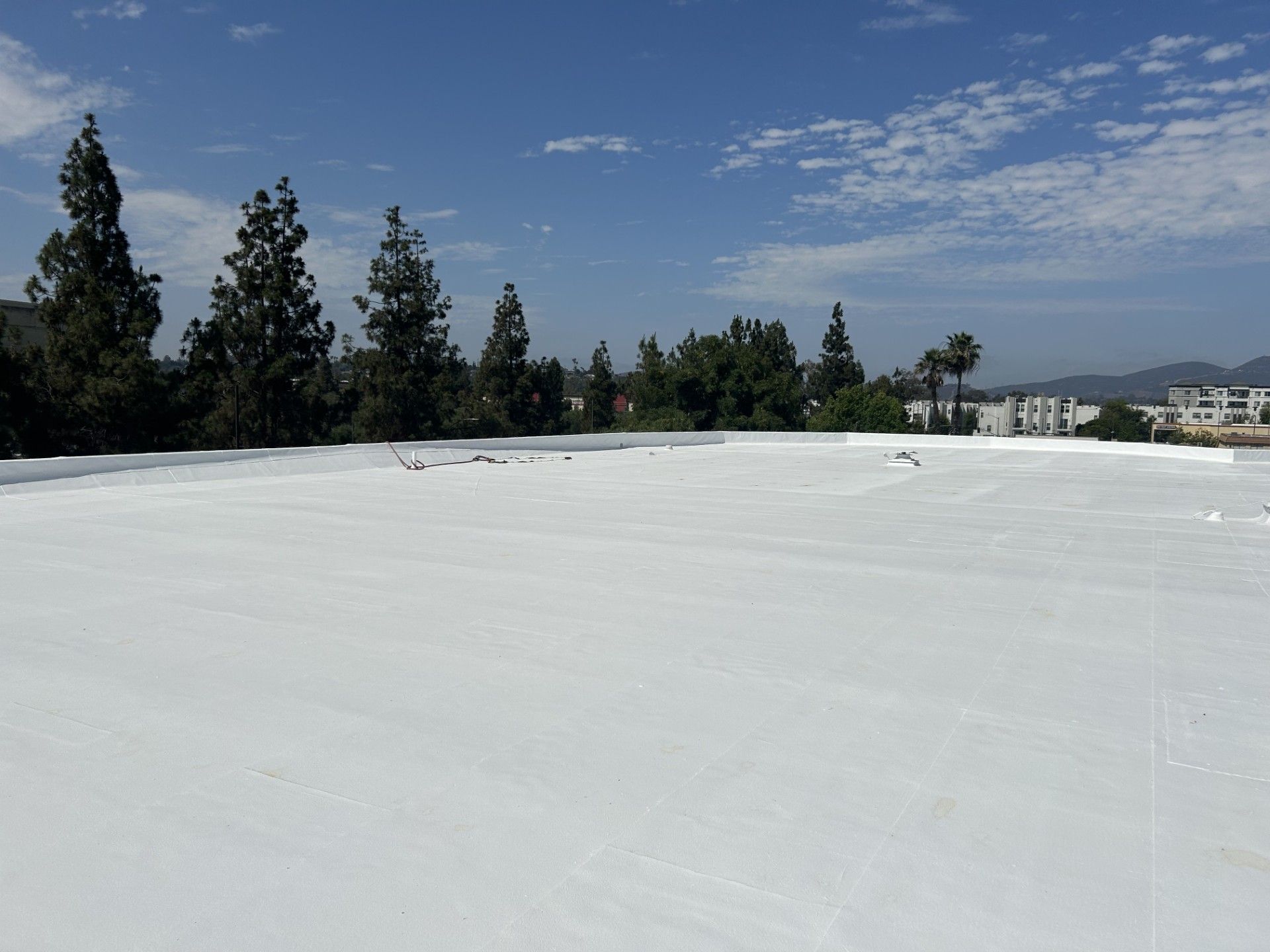 Wide white rooftop under blue sky with trees and distant hills in the background