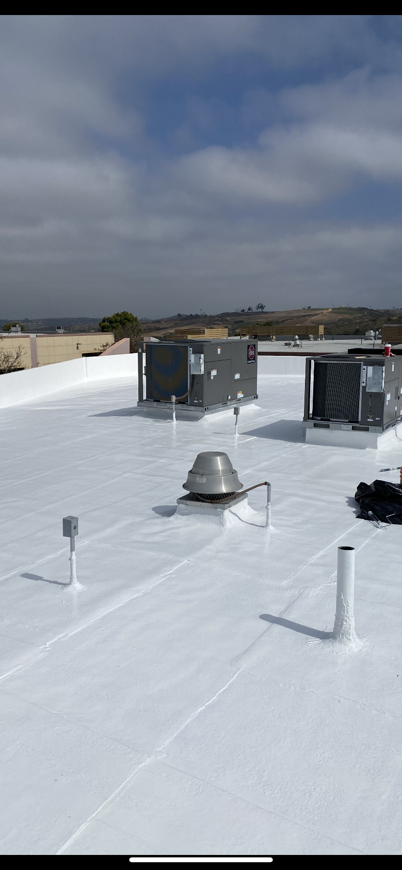 Flat white rooftop with HVAC units, vents, and a cloudy blue sky in the background