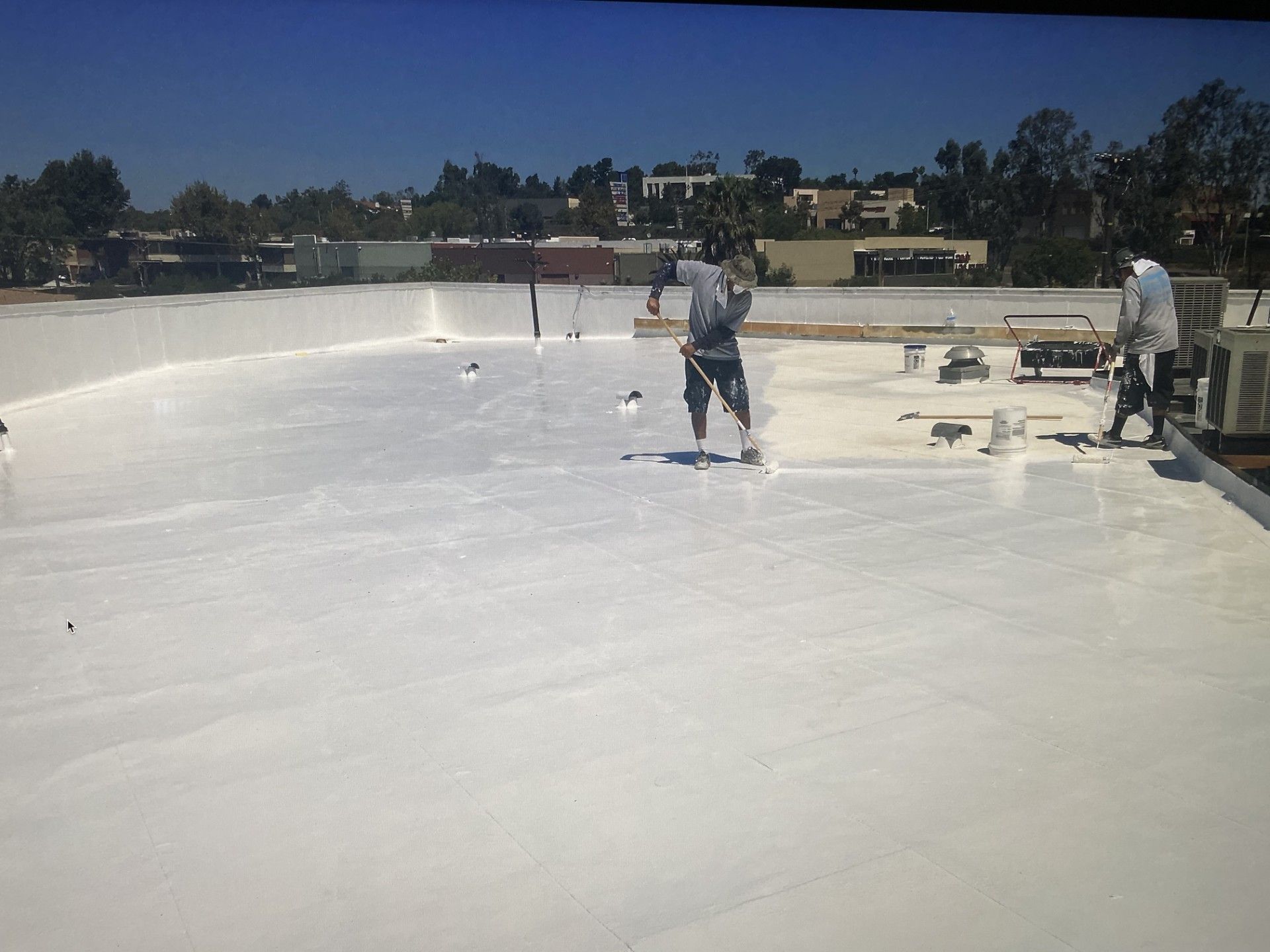 Workers applying white coating on a flat rooftop under a clear sky