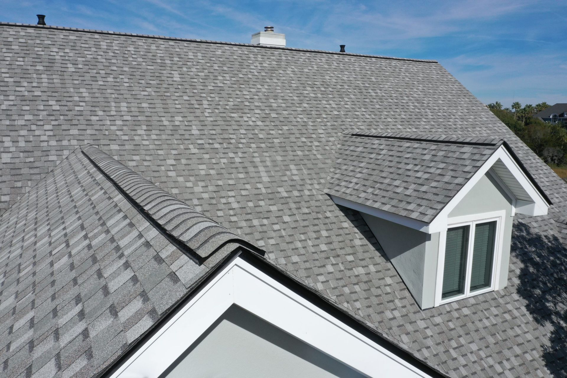 Gray shingle roof with dormer windows under a blue sky