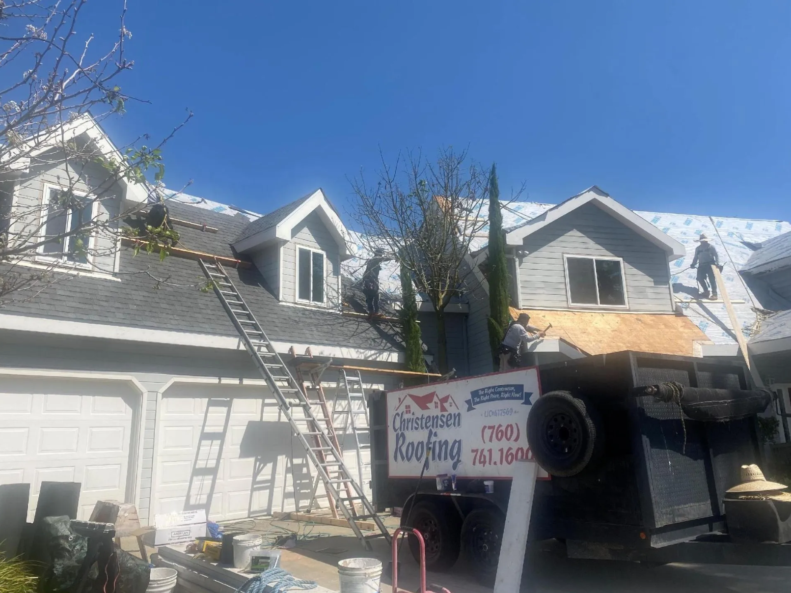 Snow-covered suburban house with a ladder and a small sign in front under a clear blue sky