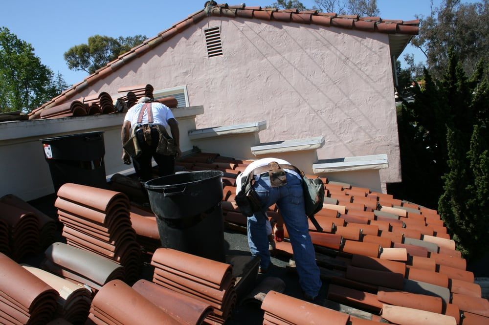 Workers installing terracotta roof tiles on a house roof with a bucket and tools