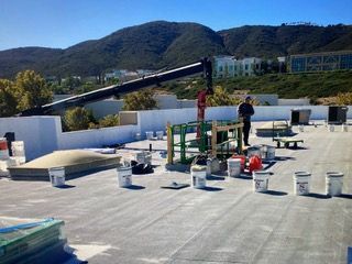 Workers on a rooftop installing equipment, with hills and buildings in the background.