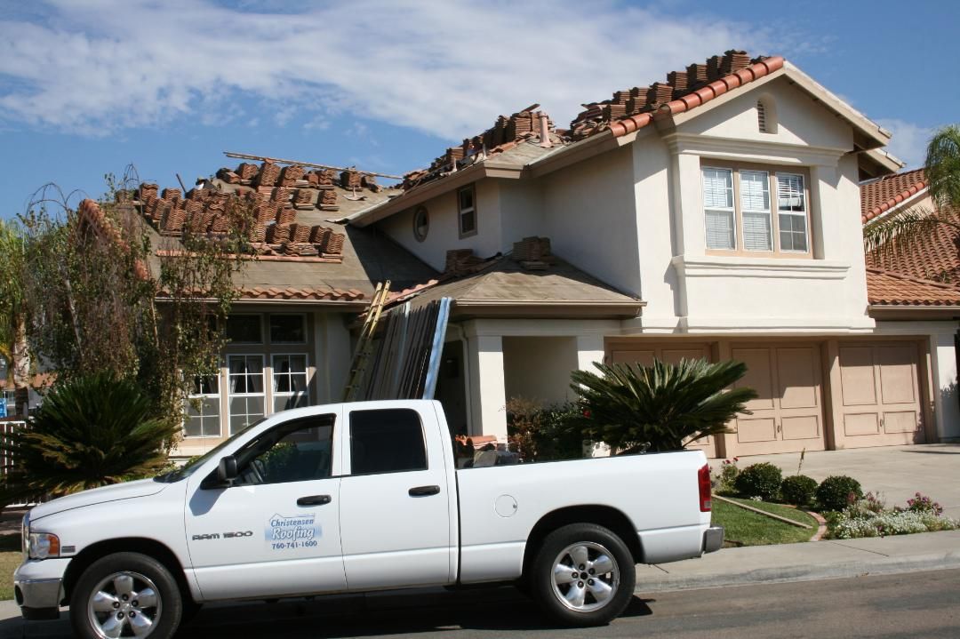 White pickup truck parked in front of a beige suburban house with a tiled roof and garage
