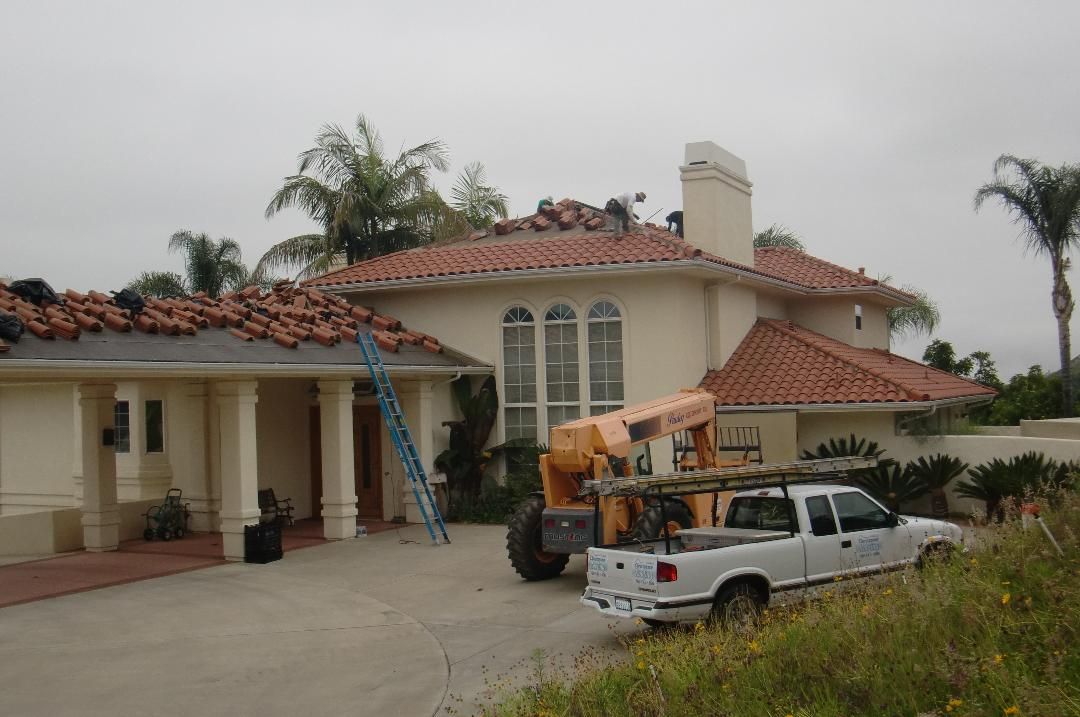 House with storm-damaged red tile roof and a utility truck parked outside