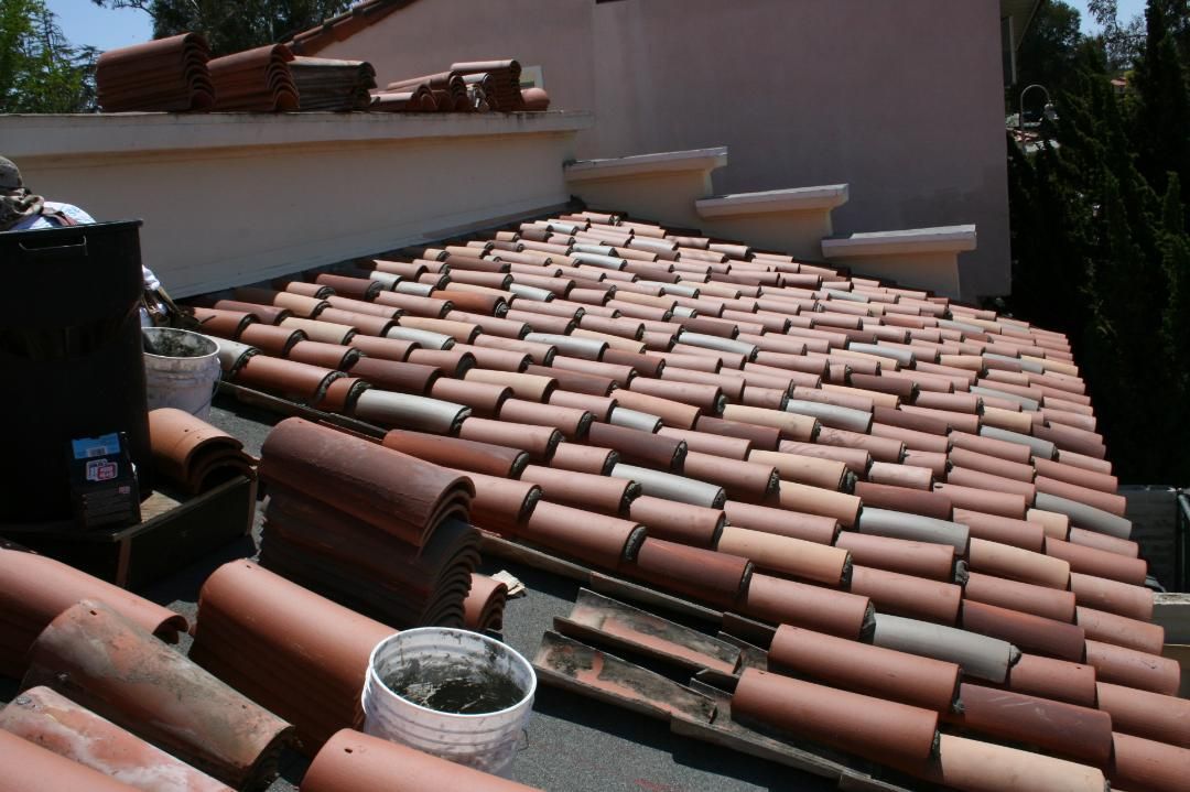 Terracotta roof tiles being installed on a house roof, with buckets and tools in the foreground