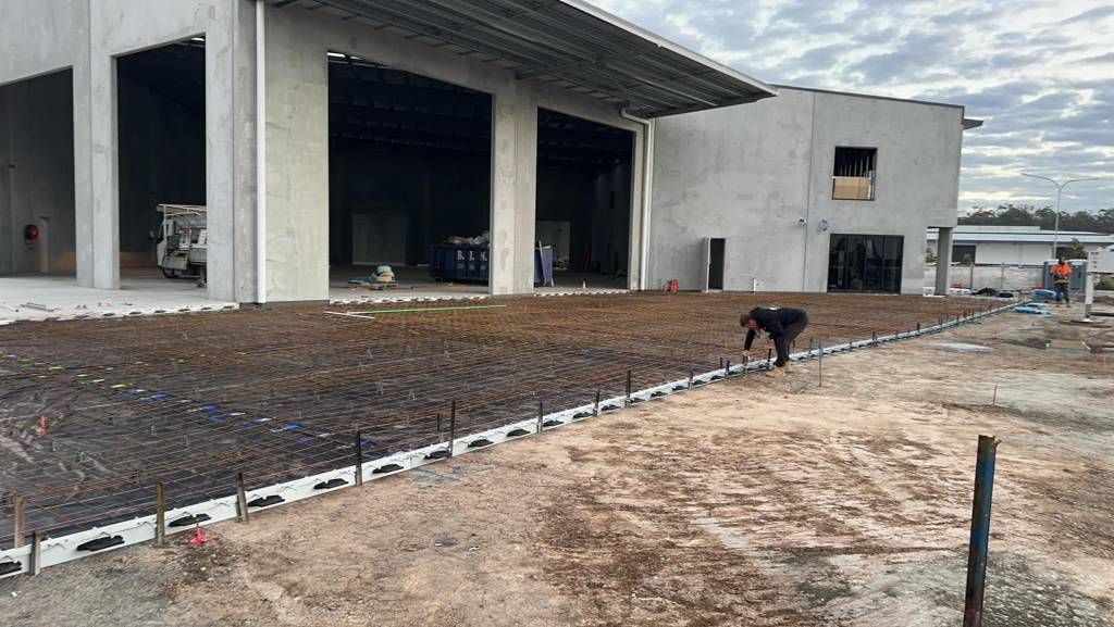 A Man is Kneeling in the Dirt in Front of a Building Under Construction — Crete to Coast Concreting in Canungra, QLD