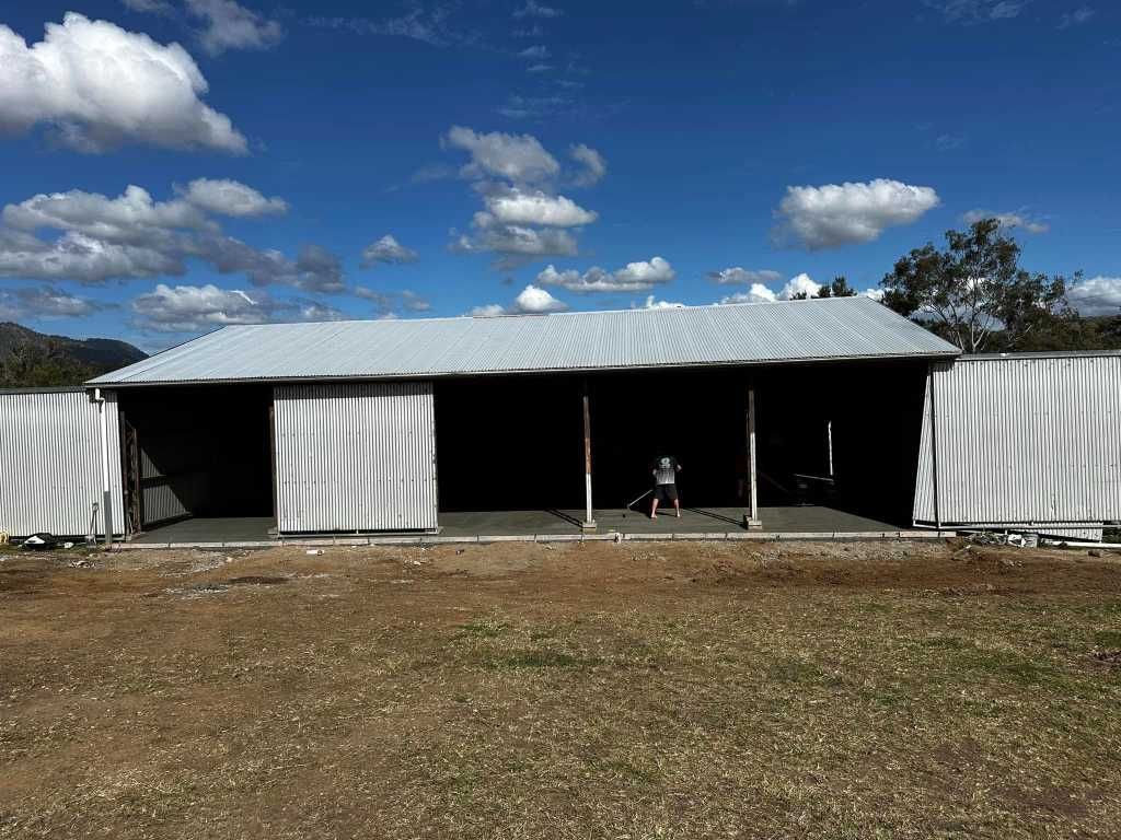 A Large White Barn is Sitting in the Middle of a Field — Crete to Coast Concreting in Browns Plains, QLD