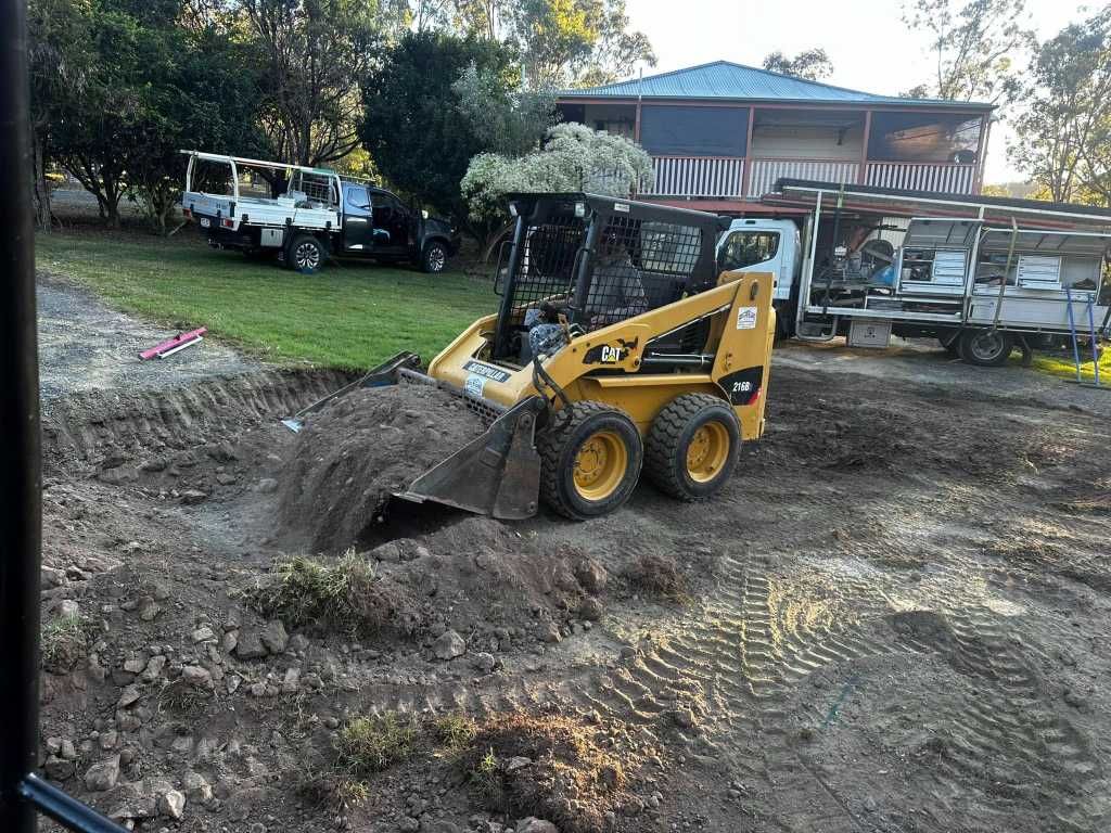 A Bulldozer is Digging a Hole in the Dirt in Front of a House — Crete to Coast Concreting in Tamborine, QLD