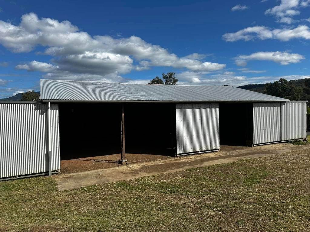 A Large Barn With Sliding Doors is Sitting in the Middle of a Grassy Field — Crete to Coast Concreting in Logan, QLD