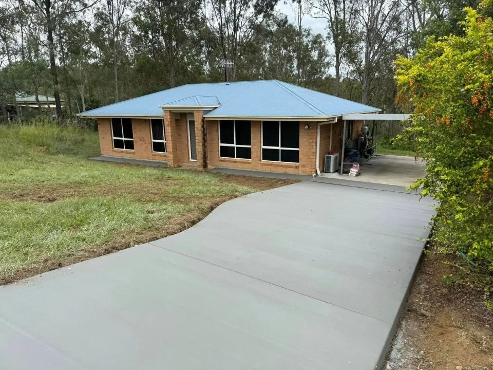 A Brick House With a Blue Roof and a Concrete Driveway Leading to It — Crete to Coast Concreting in Tamborine Mountain, QLD