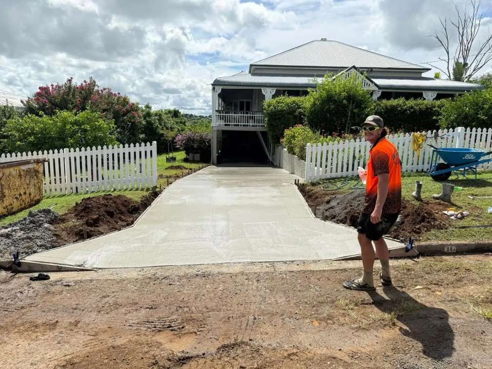 A Man is Standing on a Concrete Driveway in Front of a House — Crete to Coast Concreting in Jimboomba, QLD