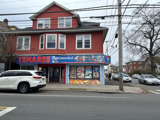 Red corner store with bright signs on a street, white SUV parked in front, winter trees and parked cars nearby